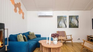 A modern living room with a blue sofa, a round wooden coffee table, a fireplace, and two paintings on the wall. - Cozy Holiday Home in Fanø near Beach (Fano)
