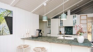 A modern kitchen with white cabinetry, a granite countertop, and pendant lighting. There are two bar stools and a vase of flowers on the counter. - Cozy Holiday Home in Fanø near Beach (Fano)