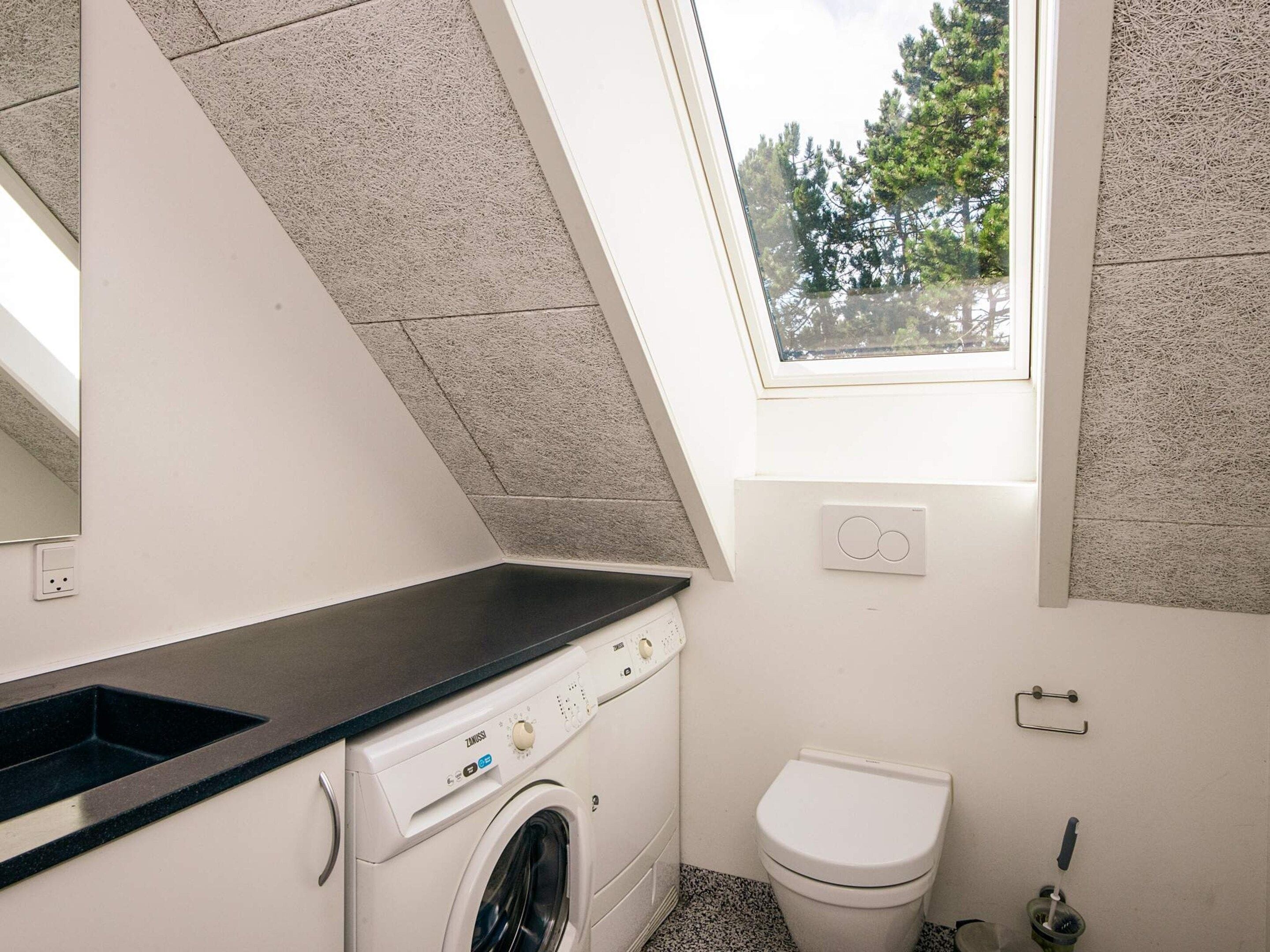 A compact laundry room with a washing machine, a sink, and a toilet.