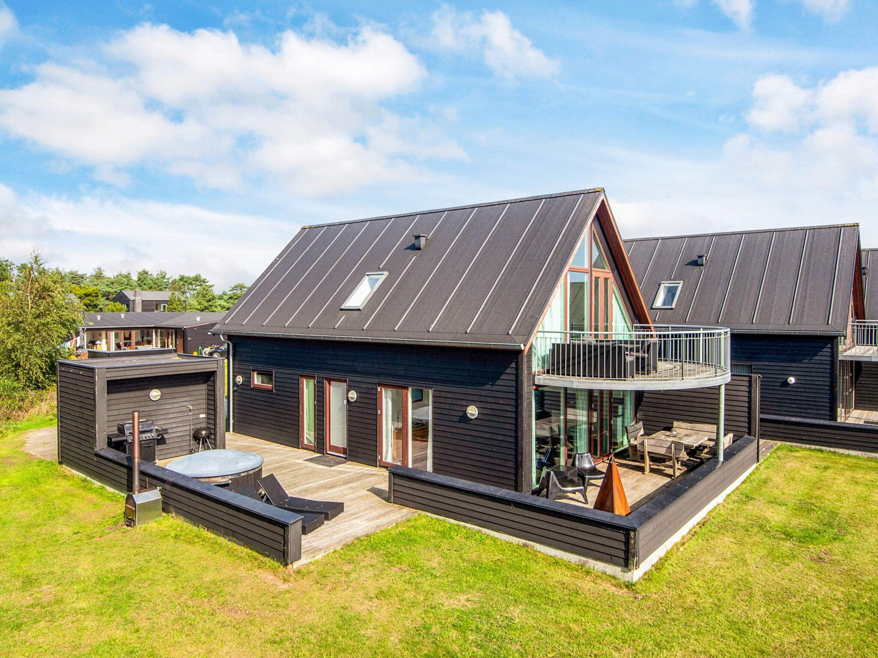 Une maison moderne à deux étages, dotée d’un toit plat, de grandes fenêtres et d’un balcon.