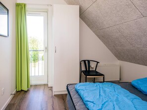 A bedroom with a bed, a chair, a radiator, and a window with curtains.