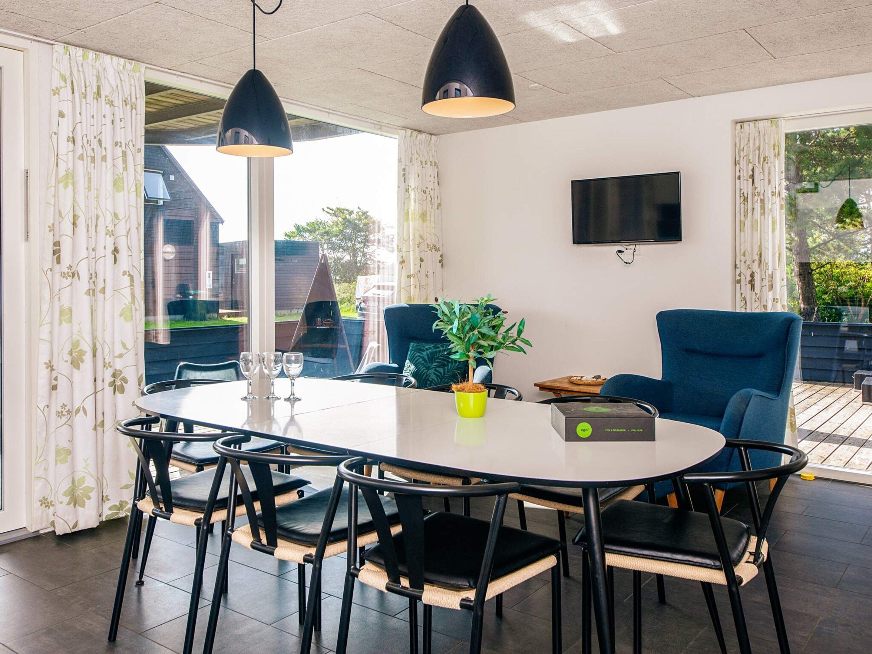 A dining area with a round table, black chairs, a potted plant, and a flat-screen TV on the wall.
