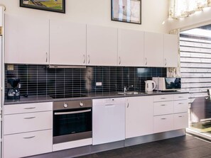 A modern kitchen with white cabinets, a black tiled backsplash, and stainless steel appliances including a coffee maker, kettle, and oven.