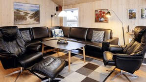 Ett modernt vardagsrum med en lädersoffa, fåtöljer, ett soffbord och en matta. Det finns tavlor på väggarna och en lampa på ett sidobord.