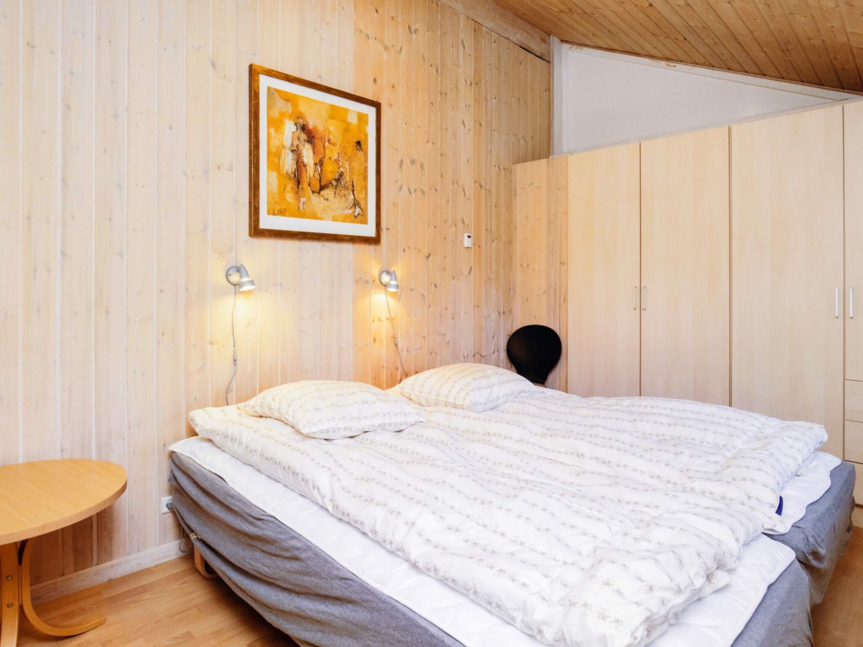 A bedroom with a bed, bedside lamps, a wooden wall, and a painting.