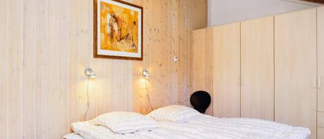 A bedroom with a bed, bedside lamps, a wooden wall, and a painting.