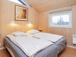 A wooden-paneled room with a bed, two wall-mounted lamps, a window with a view, and a painting on the wall. - 4 Star Holiday Home in Lokken (Lokken)
