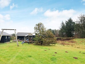 A residential area with a grassy yard, a swing set, a small shed, and a house with a tiled roof.