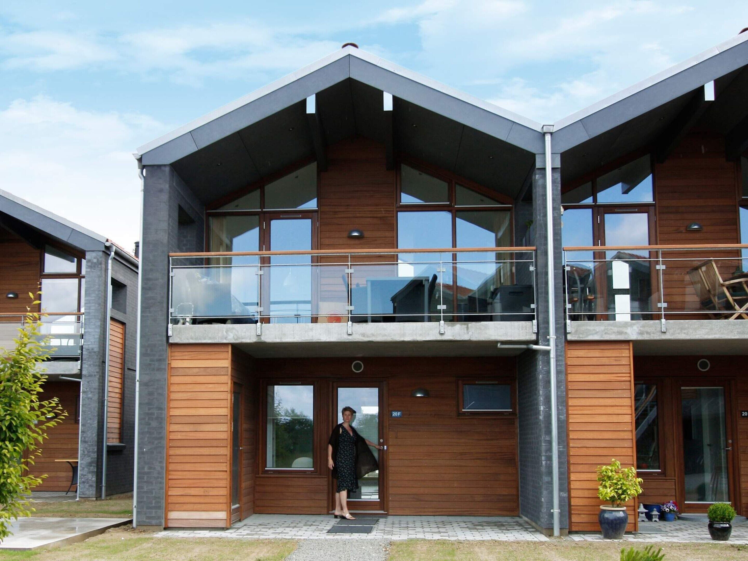 A modern two-story building with a balcony, large windows, and a wooden facade.