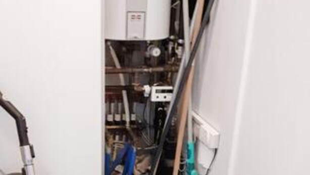 Um corredor estreito com aquecedor, tubulações e painel de controle.