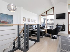 A modern living room with a staircase, a flat-screen TV, and a large window.