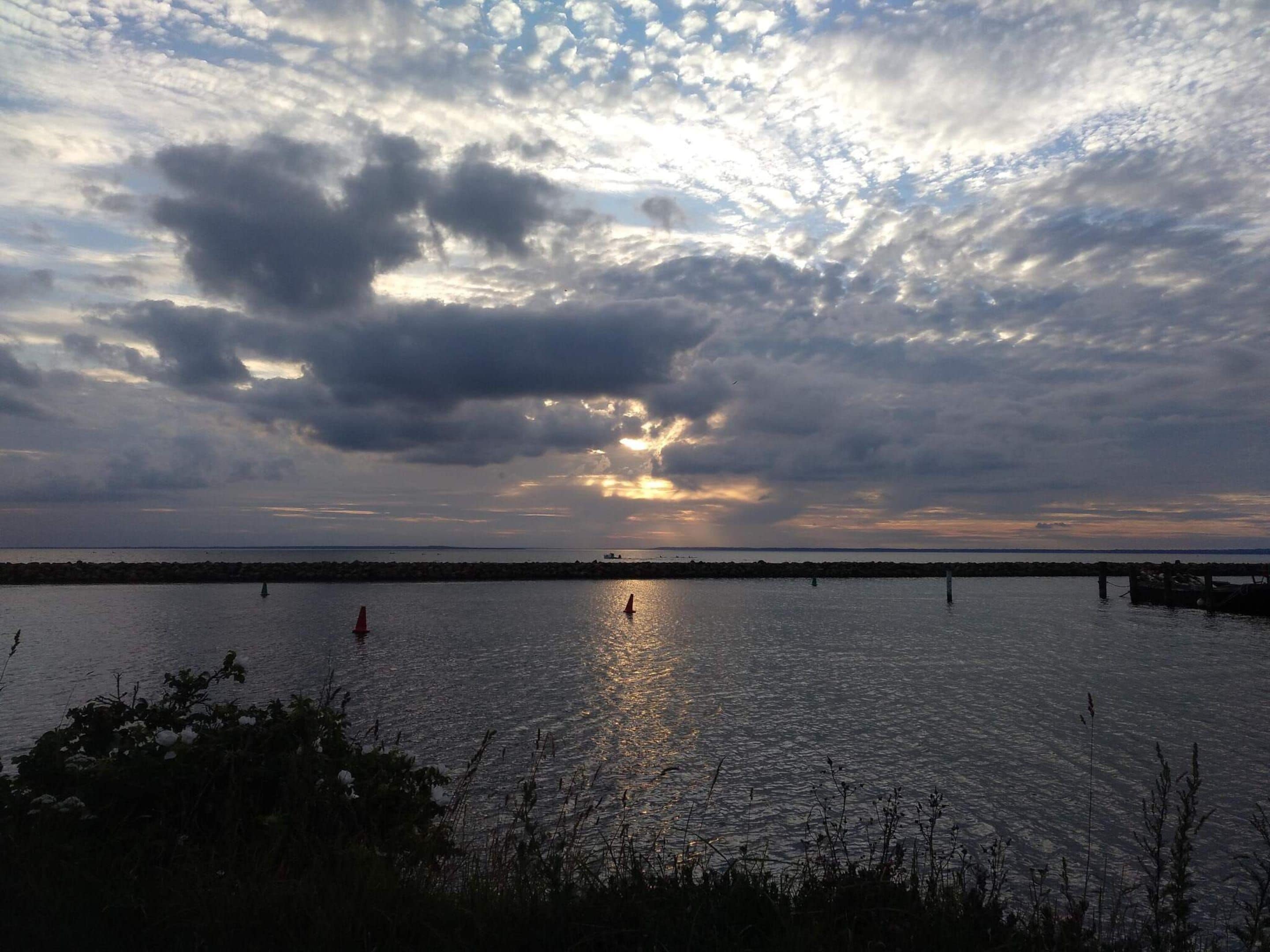 A sunset over a calm body of water with a distant shoreline and a pier.