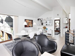 Un espacio de estar moderno con comedor, sillas de cuero negro, una mesa blanca y una estantería.