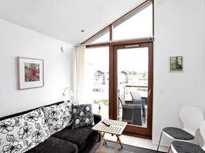 A modern living room with a sofa, a small table, and a chair. There is a large window with a view of a building outside. - 5 Star Holiday Home in Bogense (Bogense)