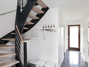 A modern interior with a black and wooden staircase, a wall-mounted coat rack, and a door leading to another room.