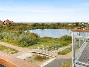 A riverside view with a wooden bridge, a glass structure, and a building with a red roof.