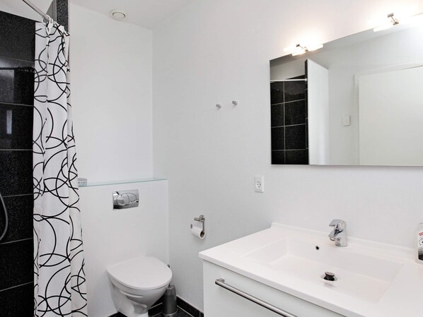 A modern bathroom with a toilet, a glass shower enclosure, a white sink with a mirror, and a black tiled wall.