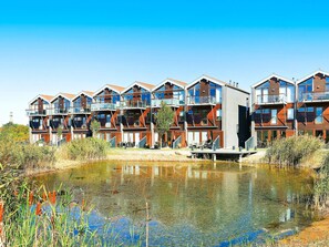 A modern multi-story residential building with balconies, a small pond in front, and a clear blue sky. - 5 Star Holiday Home in Bogense (Bogense)