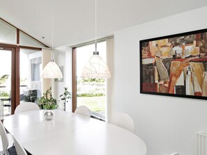 Un comedor moderno con una mesa blanca, lámparas colgantes y un cuadro abstracto grande en la pared.