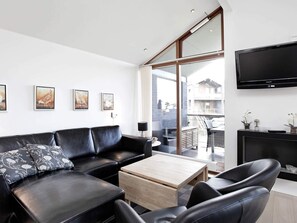 Una sala de estar moderna con un sofá de cuero negro, una mesa de centro de madera y un televisor de pantalla plana montado en la pared.