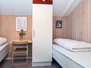 A room with a bed, a desk, a chair, a white wardrobe, and wooden walls.