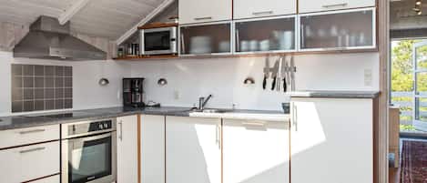 Une cuisine moderne avec des meubles blancs, un four encastré, un four à micro-ondes et une machine à café.