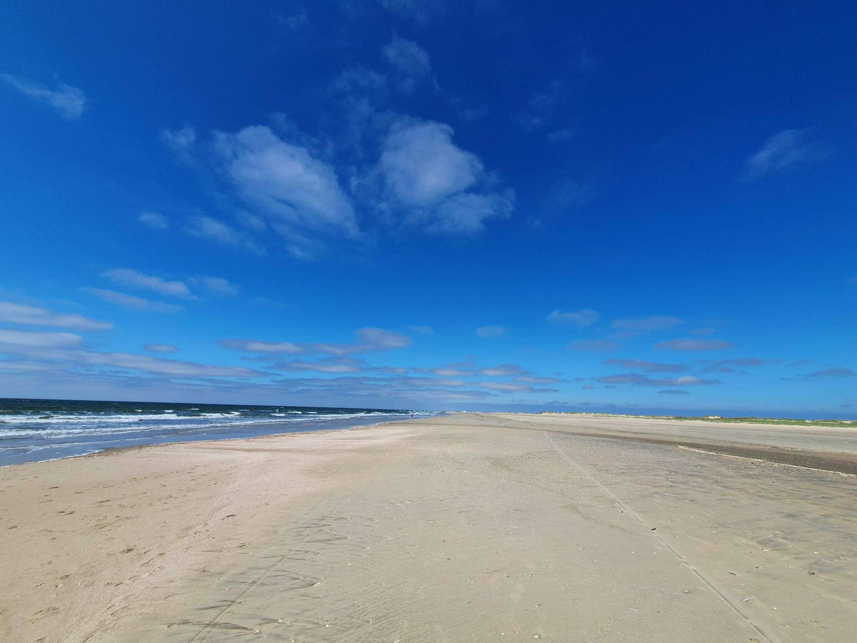 Ein weiter Sandstrand mit blauem Himmel und sanften Wellen.