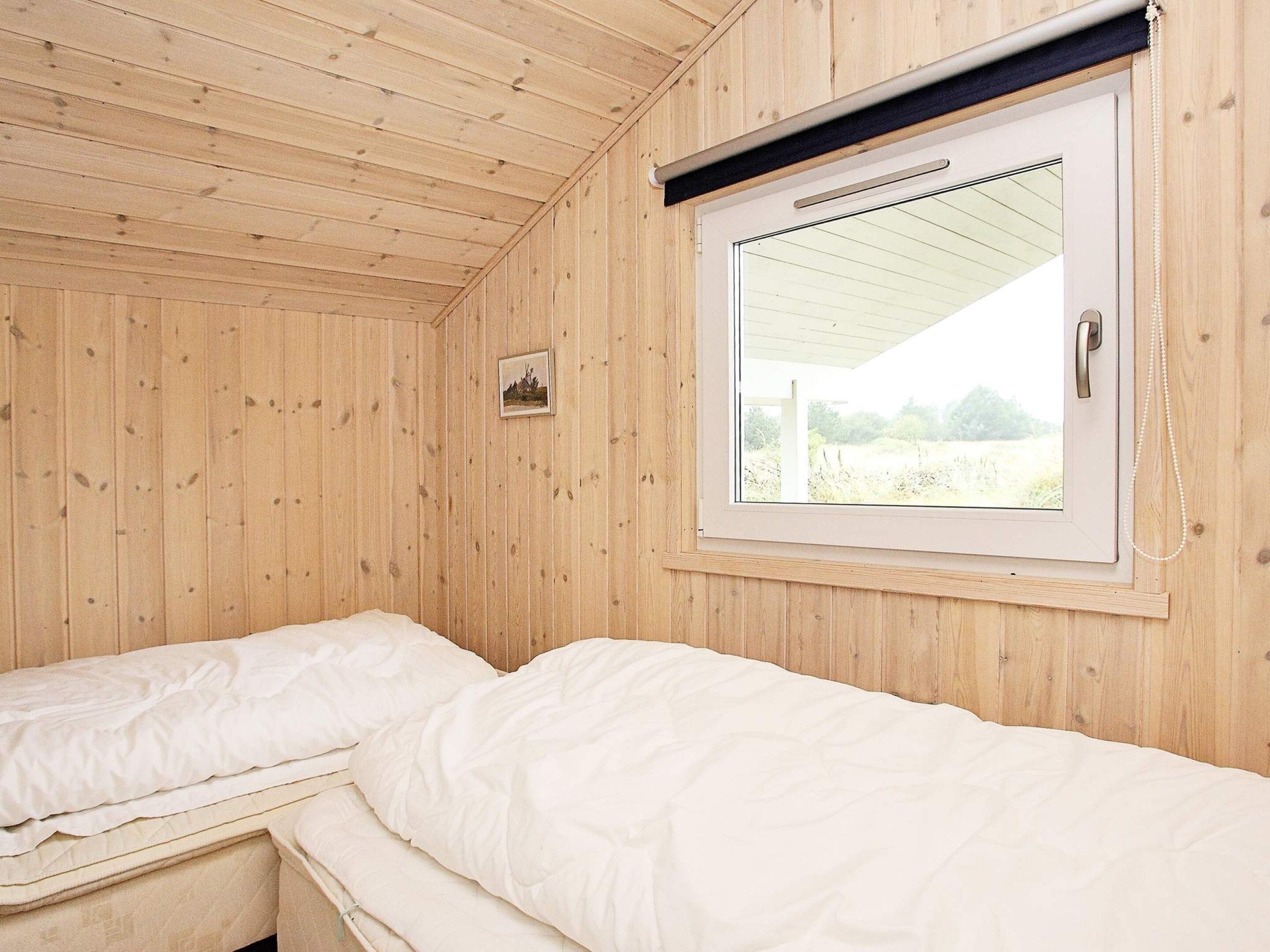 A room with wooden walls and a window with a view of a field. There are two beds with white bedding.