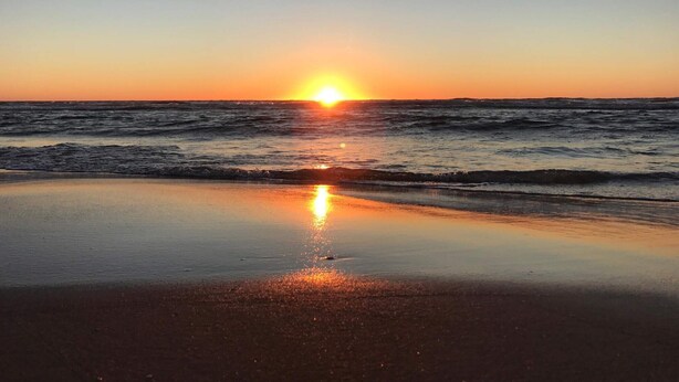 A beach with a sunset over the ocean.