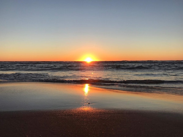 A beach with the sun setting over the ocean, reflecting on the water.
