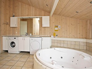 A bathroom with wooden walls, a large bathtub, and two washing machines. - 4 Star Holiday Home in Bindslev (Bindslev)