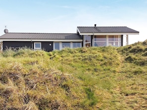 A modern house with a flat roof, large windows, and a grassy hill in the foreground.