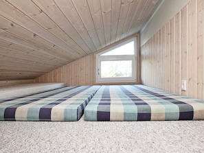 A room with a sloped ceiling and a window. There are two mattresses on the floor.