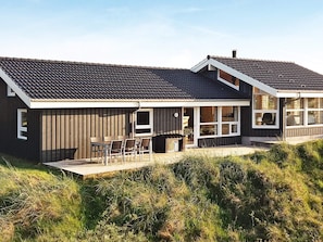A modern house with a sloped roof, large windows, and a deck with outdoor furniture.