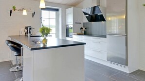 A modern kitchen with a central island, stainless steel appliances, and a large window providing natural light. - Luxury Retreat With Spa - By Traum Ferienwohnungen (Blavand)
