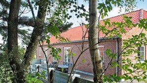 A brick building with a red-tiled roof, surrounded by trees and a metal fence. - Luxury Retreat With Spa - By Traum Ferienwohnungen (Blavand)