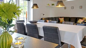 A modern dining area with a long table, chairs, and pendant lighting. - Luxury Retreat With Spa - By Traum Ferienwohnungen (Blavand)