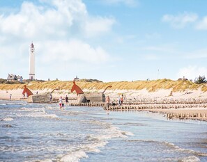 Una playa con un faro, dunas y un muelle de madera.