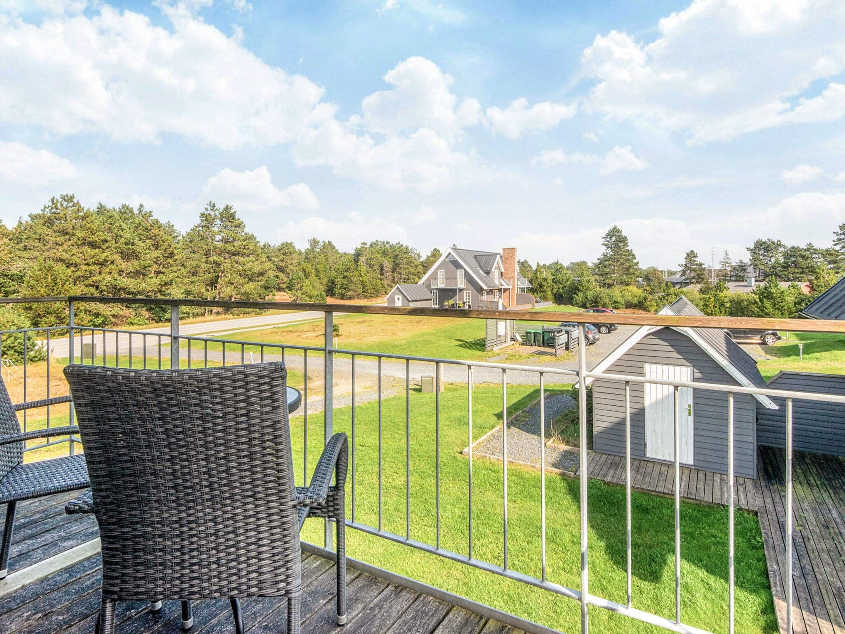 A balcony with wicker furniture overlooking a residential area with houses and a road.