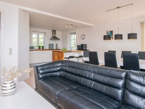 A modern kitchen with white cabinets, a wooden island, and a dining area with a black leather sofa and dining table.