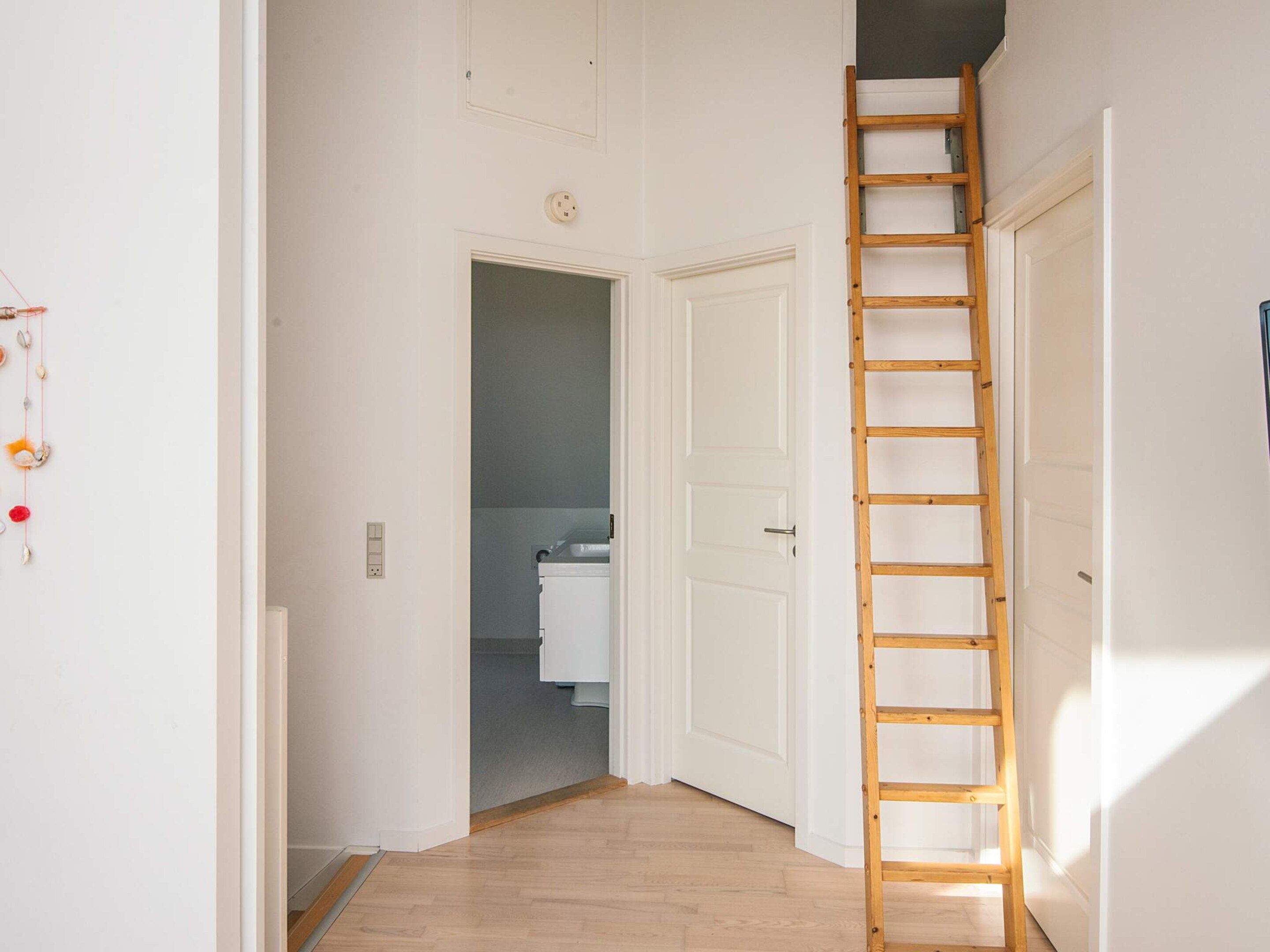 A hallway with a wooden ladder, a white door, and a visible bathroom in the background.
