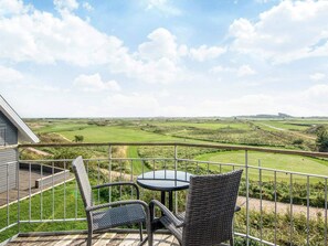 A balcony with wicker chairs and a table, overlooking a green landscape.