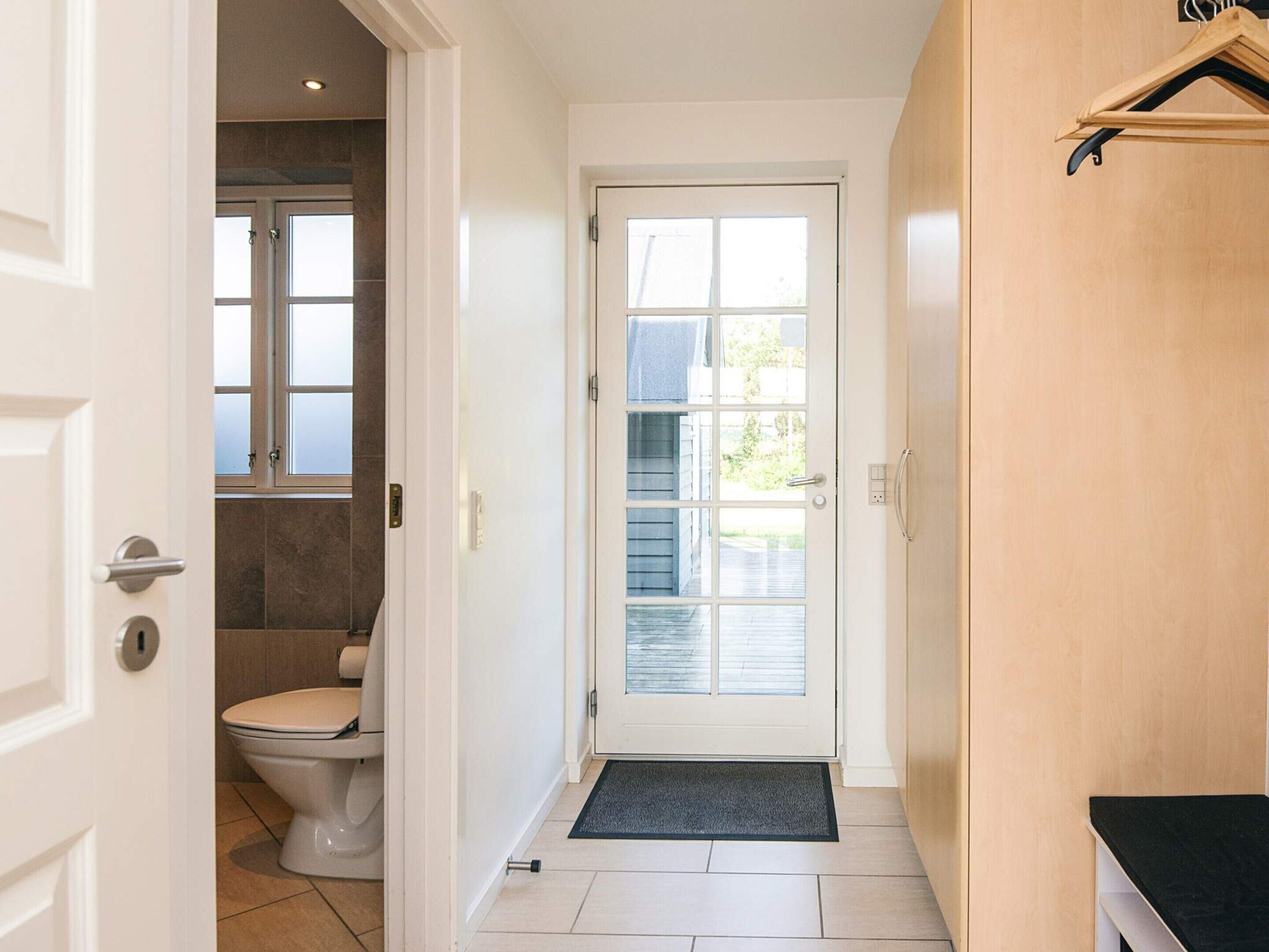 A hallway leading to a bathroom with a toilet, a window, and a door.