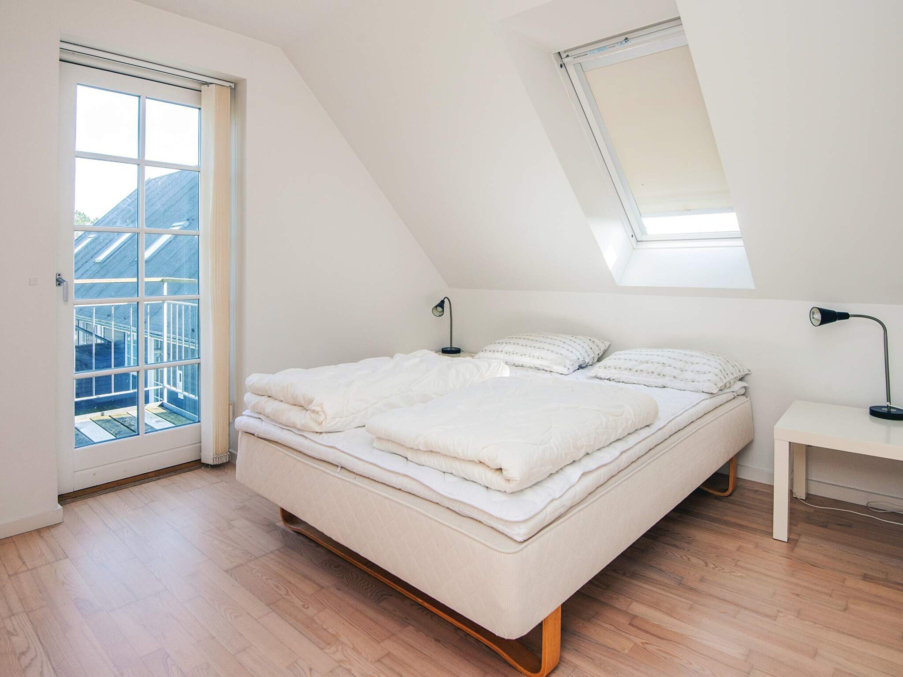 A bedroom with a bed, a bedside table, a lamp, a window, and a skylight.