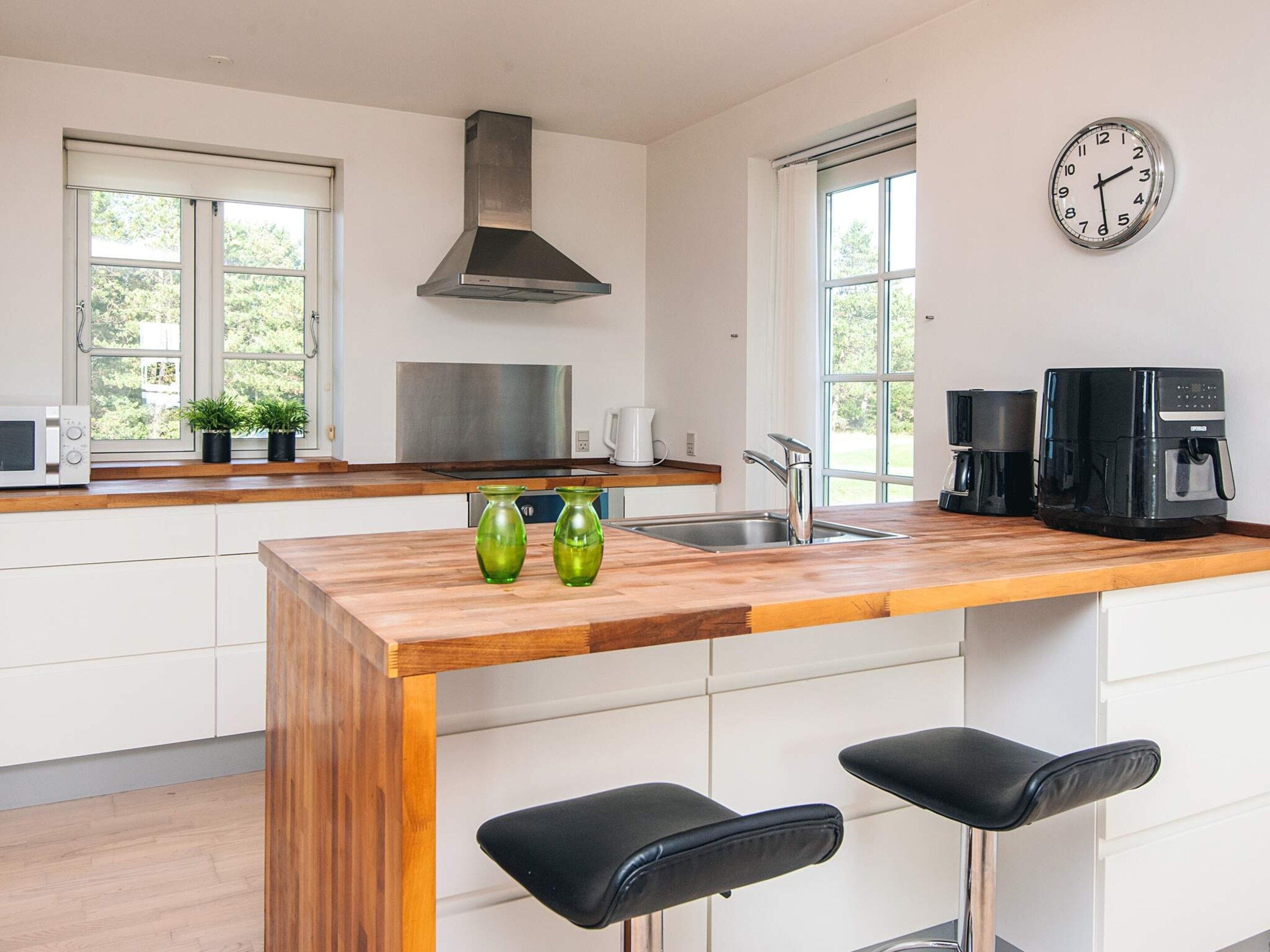 A modern kitchen with a wooden island, stainless steel appliances, and a clock on the wall.