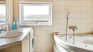 A bathroom with a window, a sink, a washing machine, and a bathtub. - 5 Star Holiday Home in Storvorde (Storvorde)