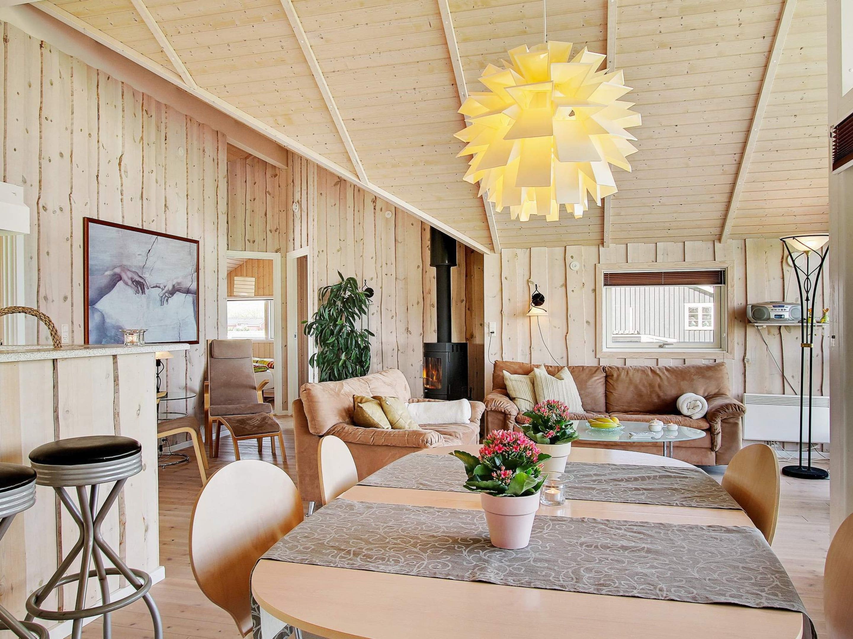 A cozy living room with a fireplace, wooden walls, a dining area, and a large window.
