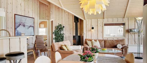 Una sala acogedora con chimenea, paredes de madera, una zona de comedor y un ventanal grande.