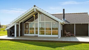 A modern house with a sloped roof, large windows, and a wooden deck. - 5 Star Holiday Home in Storvorde (Storvorde)