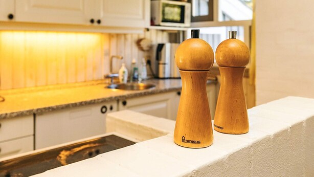 Una cocina con armarios blancos, un microondas y saleros y pimenteros de madera sobre una encimera.